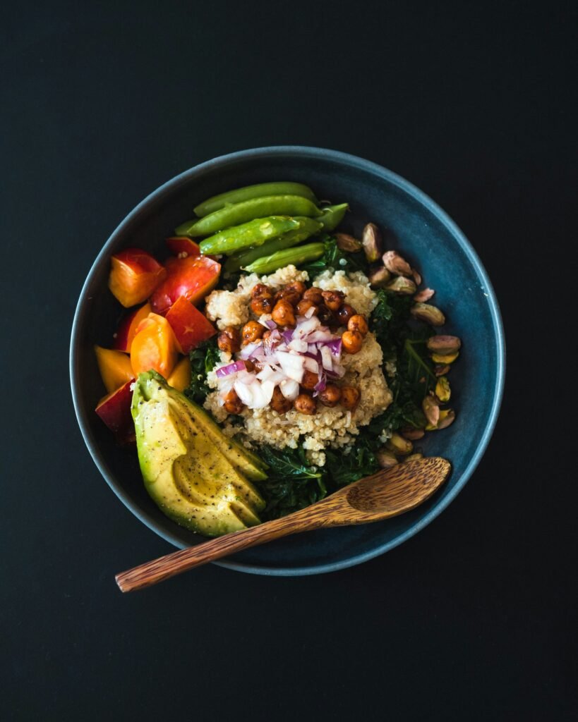 Colorful vegetarian quinoa appetizer bowl with avocado, chickpeas, tomatoes, greens, pistachios, and snap peas.