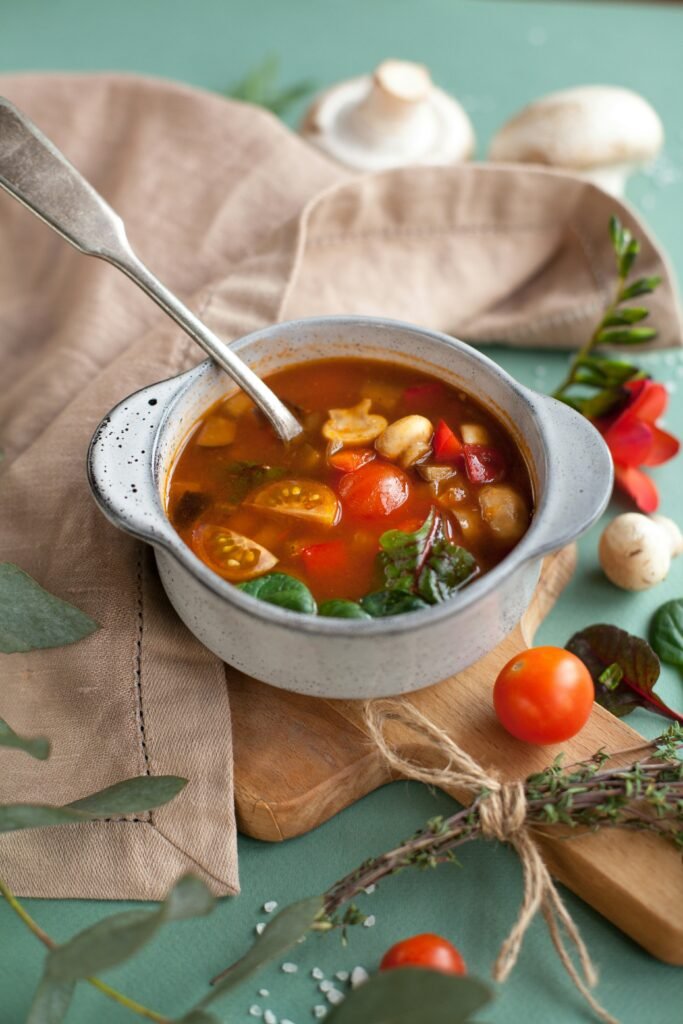 Warm vegetarian vegetable soup with tomatoes, mushrooms, leafy greens, and herbs served in a small bowl.