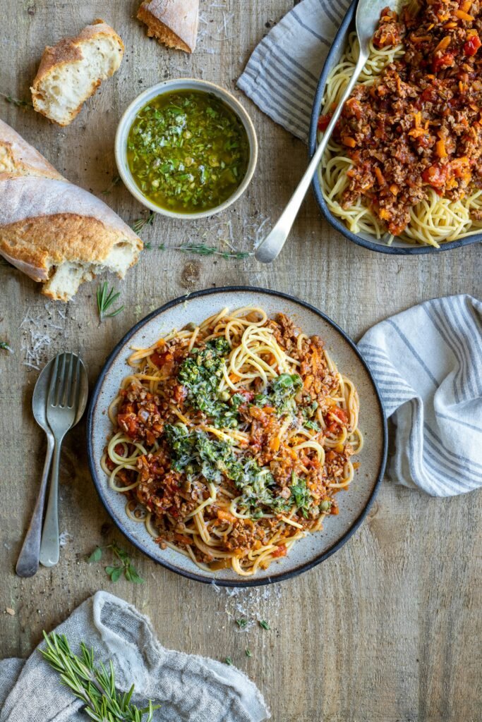 Vegetarian pasta appetizer with tomato vegetable sauce, herb topping, crusty bread, and olive oil dip.