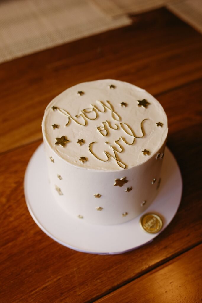 Pink and blue gender reveal cake with baby topper, clouds, baby feet, cupcakes, and Boy or Girl sign.